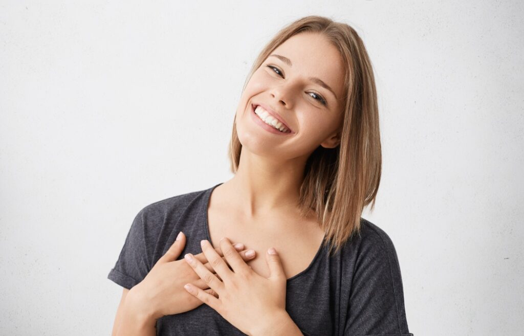The Surprising Link Between Your Oral Health and Your Heart 11 Beautiful positive friendly-looking young mixed race woman with lovely sincere smile feeling thankful and grateful, showing her heart filled with love and gratitude holding hands on her breast